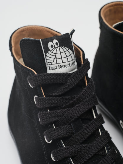 Close-up of a black suede high-top sneaker with black laces and a white tongue label featuring a cartoon face and the text 'Last Resort 48'.