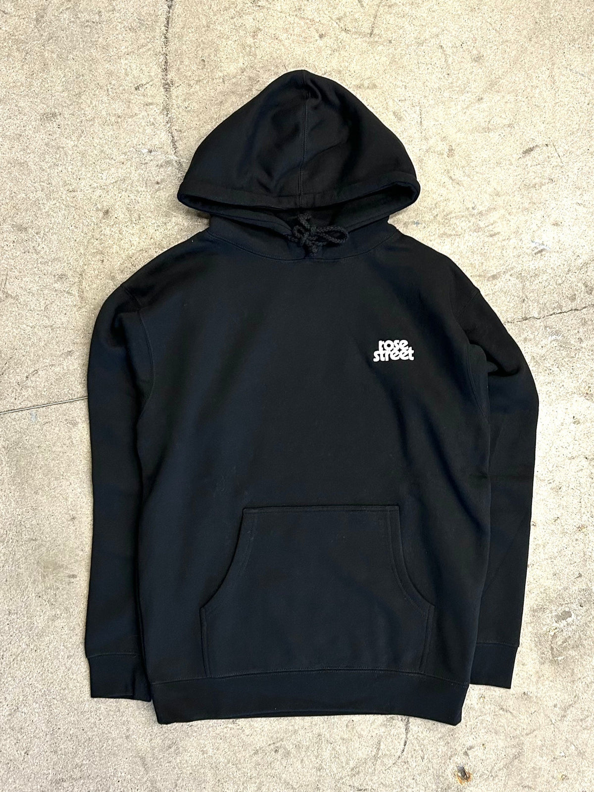 Black hoodie with a logo on the chest against a textured beige background