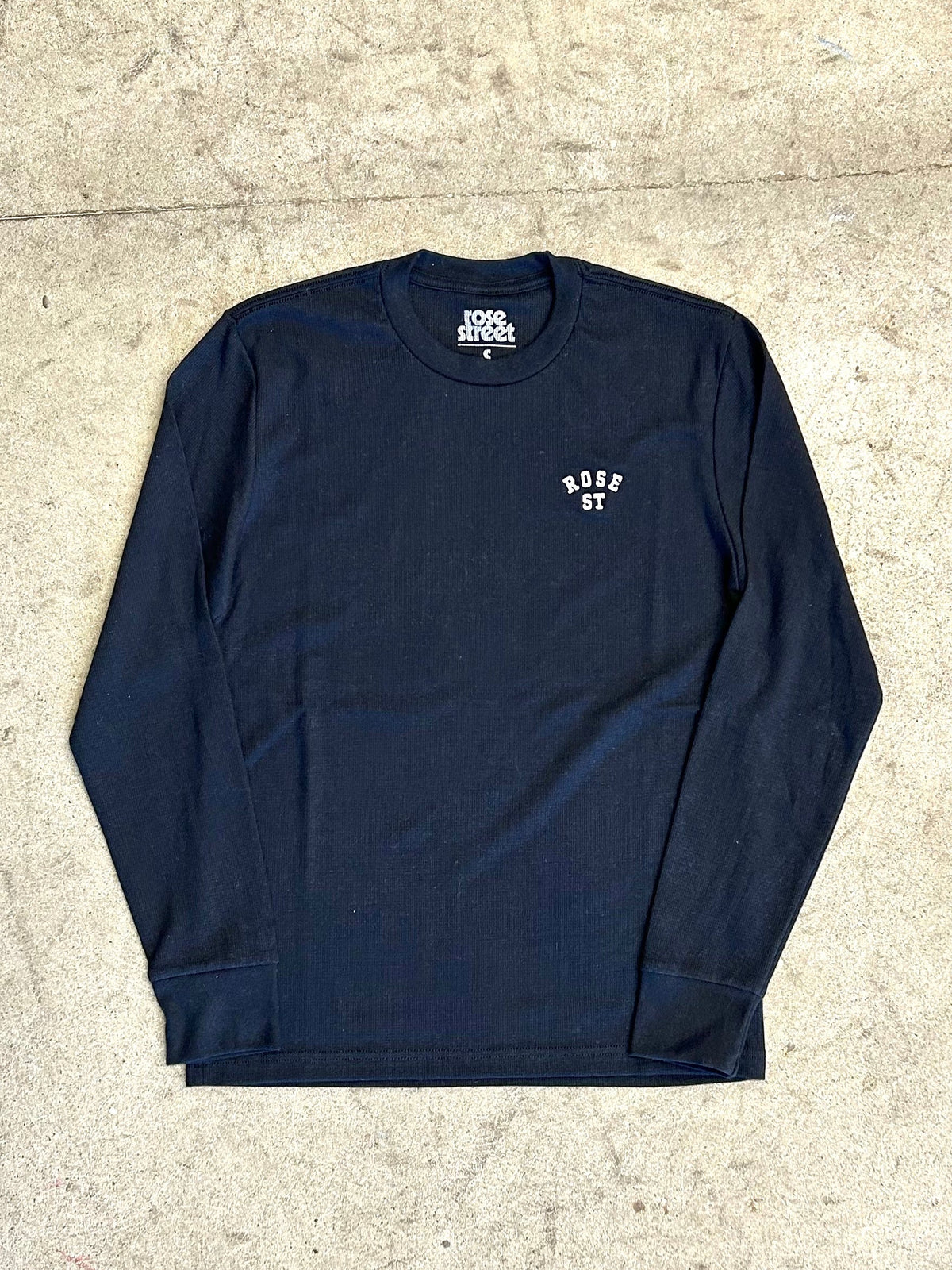 Navy long-sleeve shirt with white text on a beige concrete floor