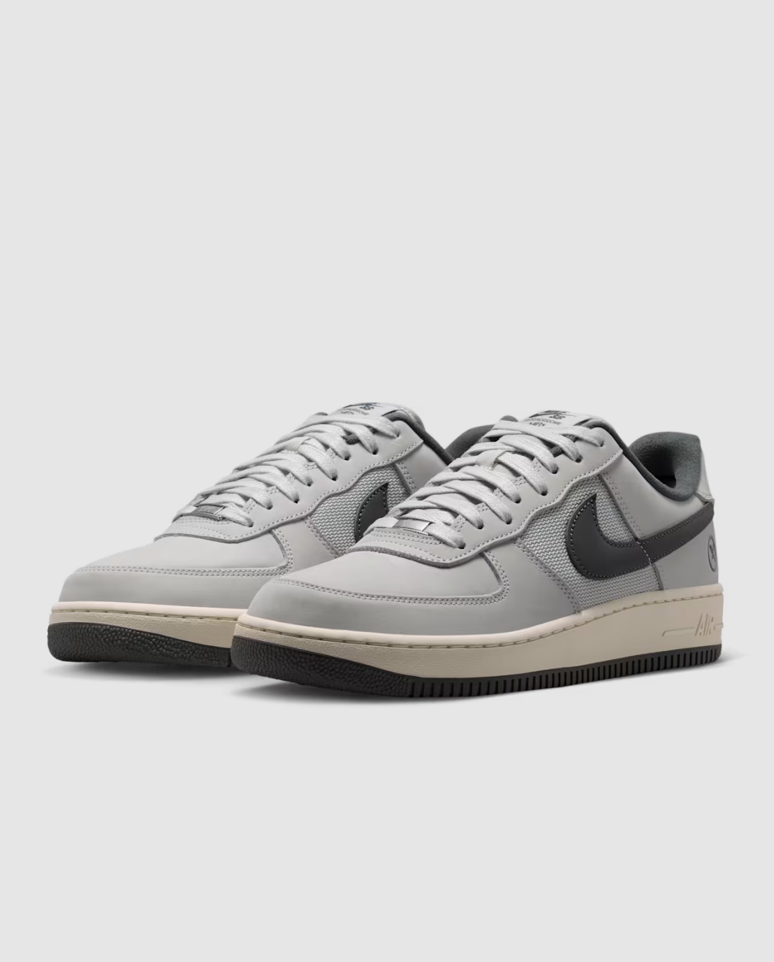 A pair of Nike Air Force 1 Low sneakers in light gray suede and mesh with dark gray Swooshes, cream midsoles, and black rubber soles, photographed on a light gray studio background.