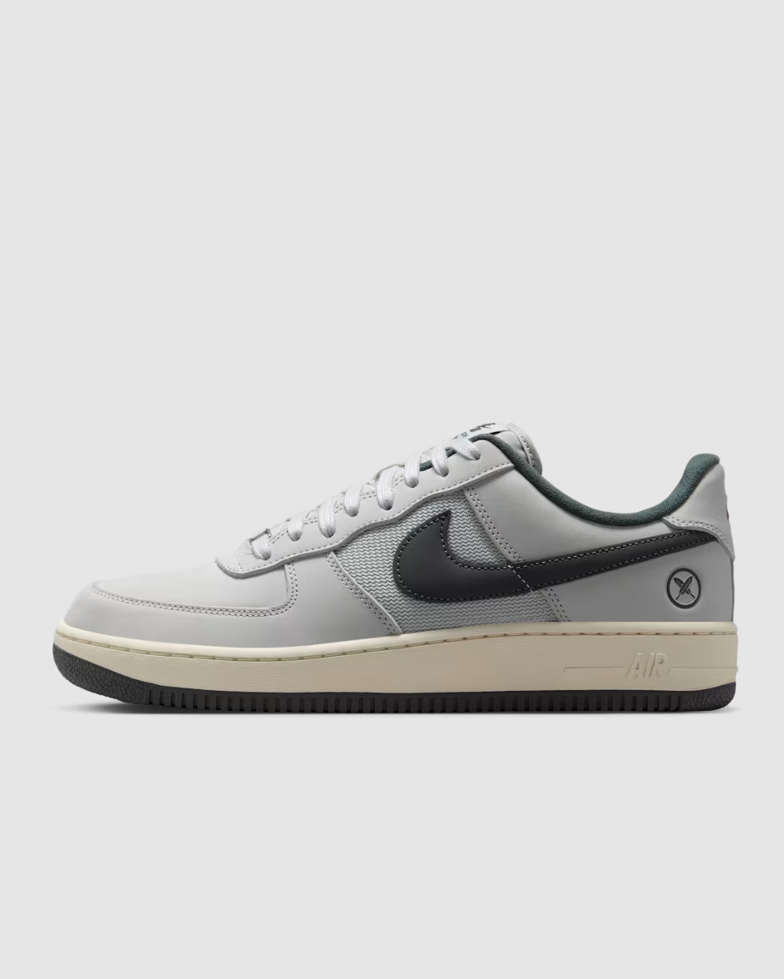 A Nike Air Force 1 Low sneaker in light gray and black, featuring a light gray leather and mesh upper, a black Swoosh, a cream-colored midsole, and a black outsole, shown against a light gray background.