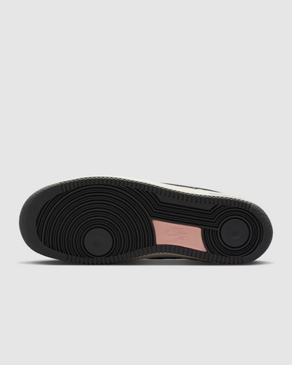 A top-down view of a sneaker's black textured rubber sole, featuring circular tread patterns and a light pink heel insert, shown against a plain white background.